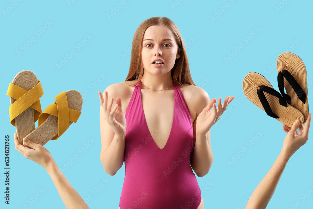 Helpless young woman and hands with flip-flops on blue background