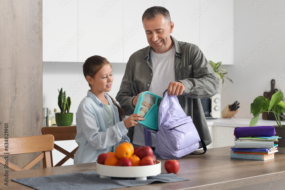 Father helping his little daughter to pack schoolbag in kitchen