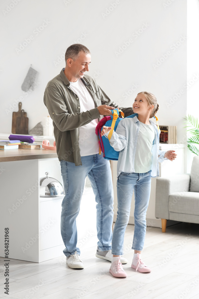 Father putting schoolbag on his little daughter in kitchen