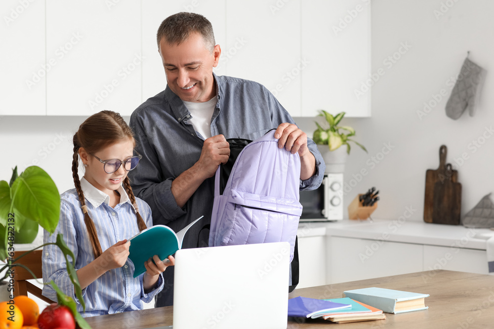 Father helping his little daughter to pack schoolbag in kitchen