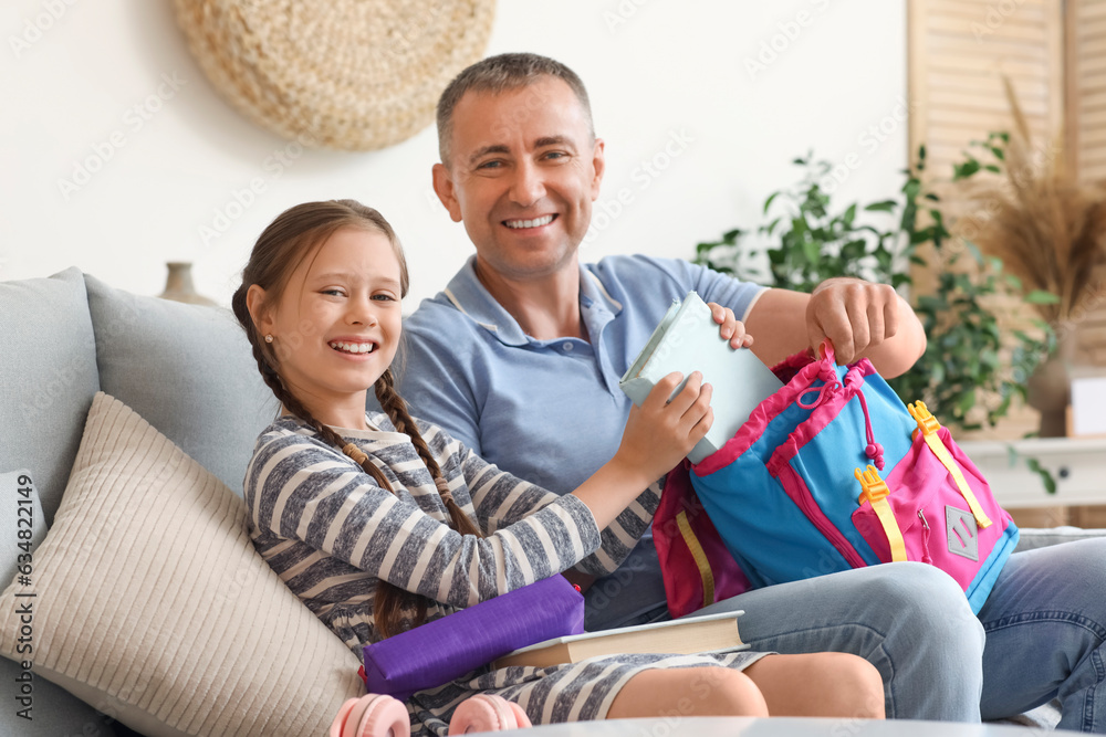 Father helping his little daughter to pack schoolbag at home