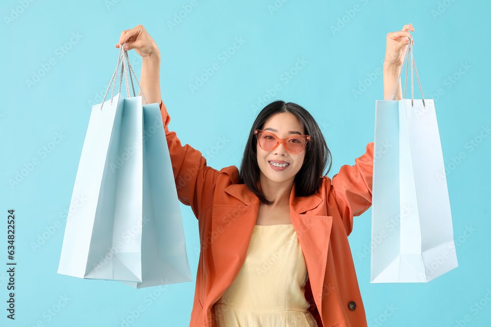 Happy beautiful young Asian woman with shopping bags on blue background