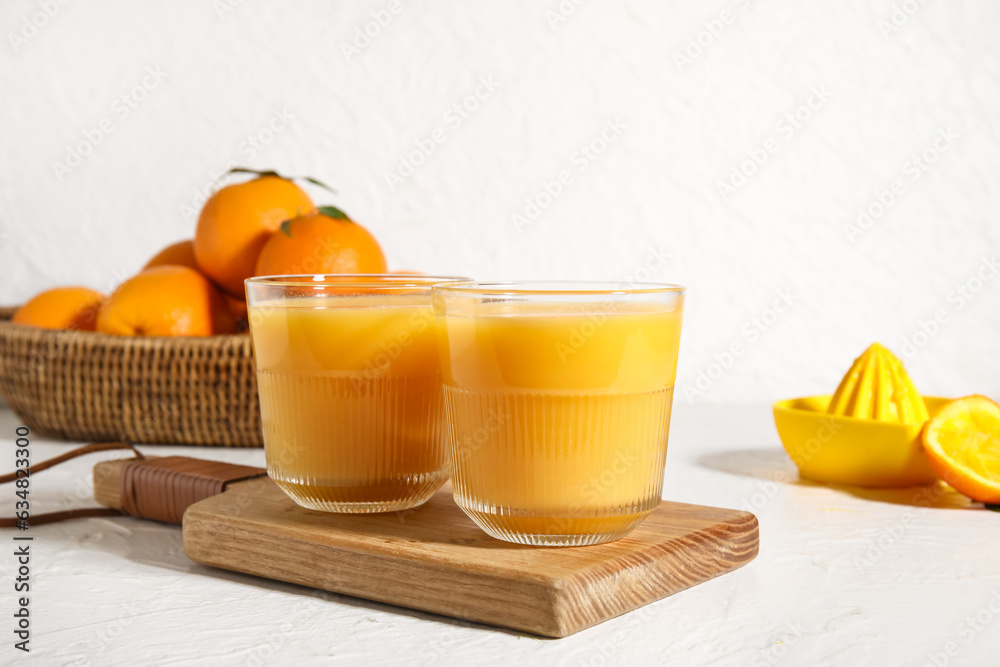 Wooden board with glasses of fresh orange juice on white background