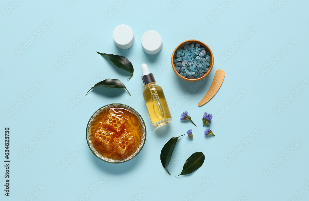 Bottle and jars of cosmetic products with sea salt on blue background