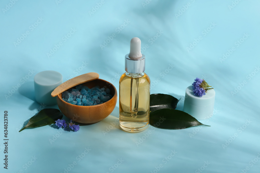 Bottle and jars of cosmetic products with sea salt on blue background