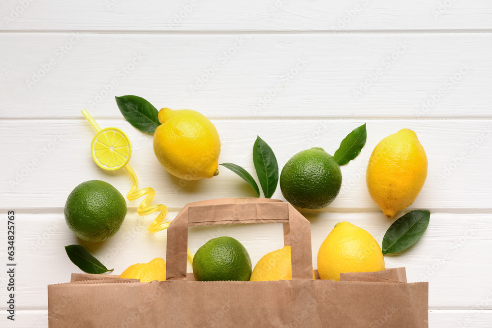 Paper bag with fresh lemons and limes on white wooden background