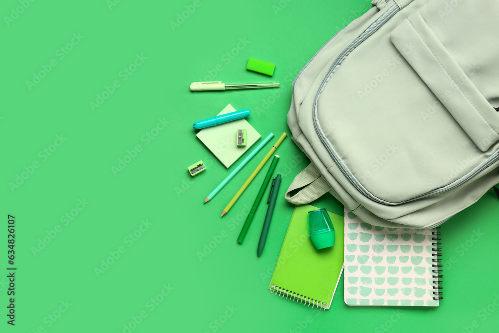 Stylish school backpack with different stationery supplies on green background