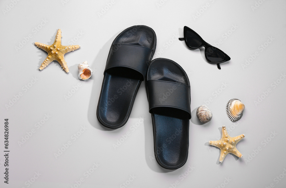 Female stylish flip flops with sunglasses and seashells on beige background