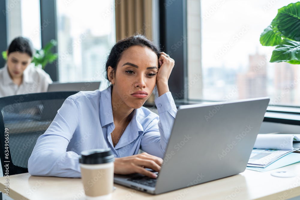 Exhausted Latino young businesswoman overworking in office workplace. 