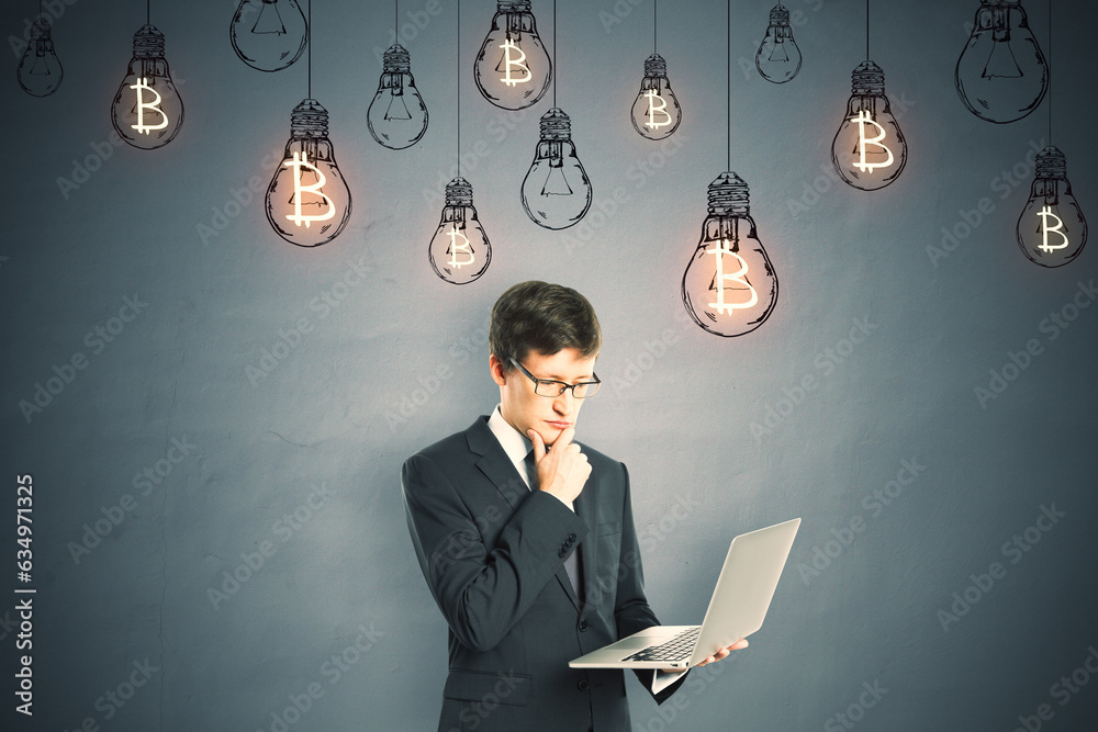 Portrait of a young businessman with a laptop in his hands standing in front of a gray wall with glo