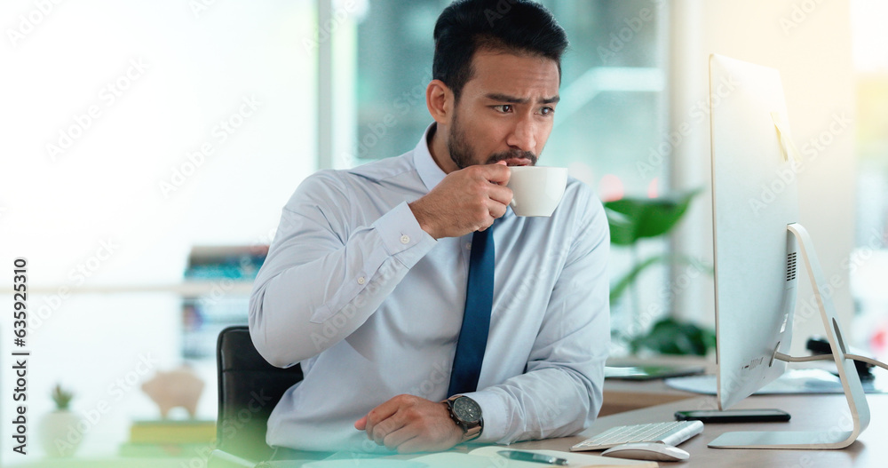 Exhausted businessman typing on a computer working and sipping coffee in a corporate office. A male 