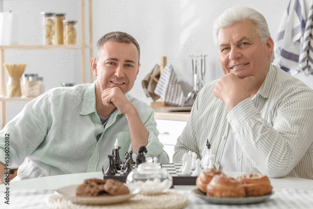 Mature brothers playing chess at table in kitchen