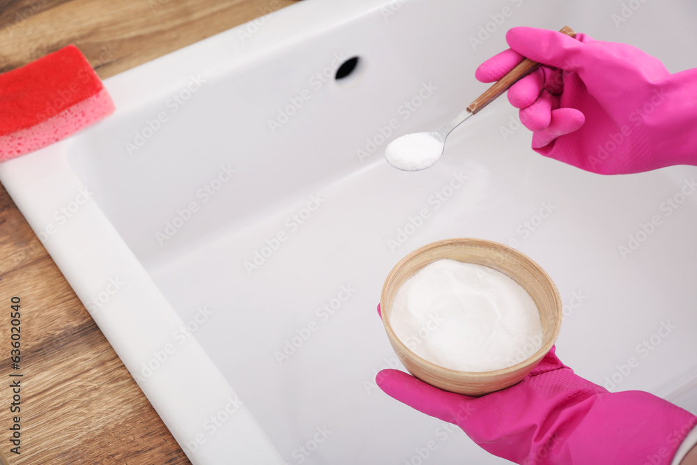 Woman in rubber gloves cleaning white sink with baking soda, closeup