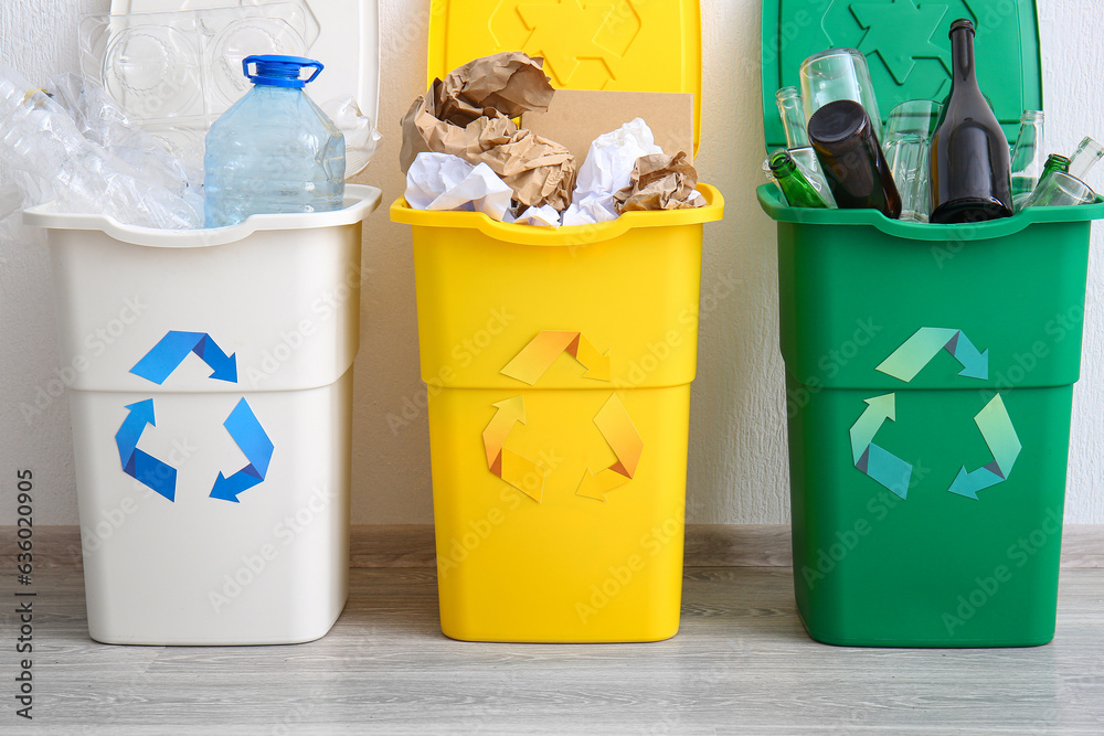 Trash bins with recycling symbol and different garbage near white wall