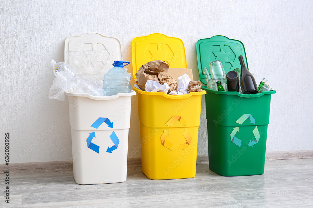 Trash bins with recycling symbol and different garbage near white wall