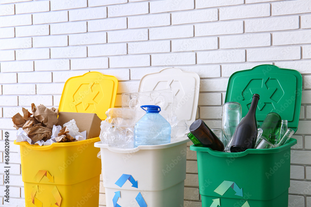 Trash bins with recycling symbol and different garbage near white brick wall