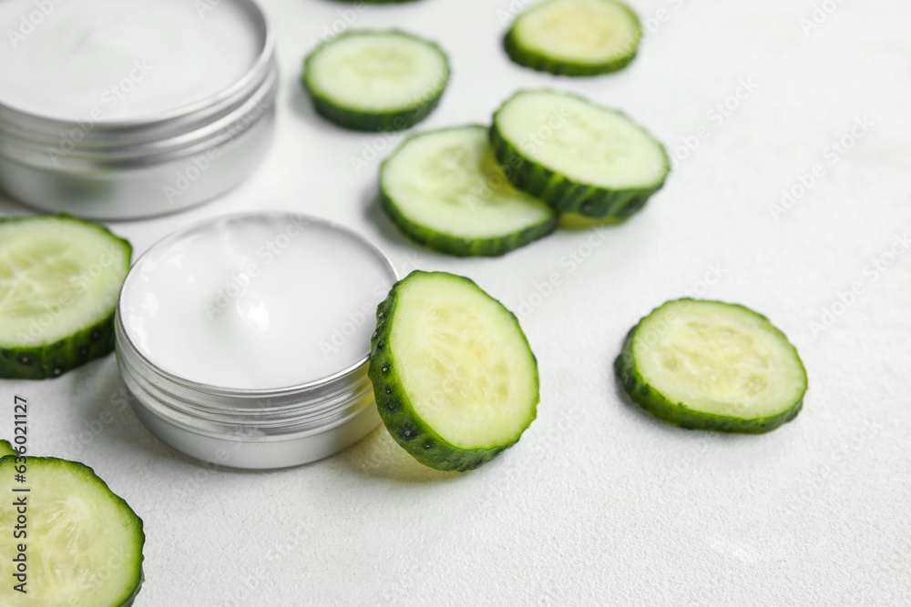 Jars of natural cream and cucumber slices on light background, closeup