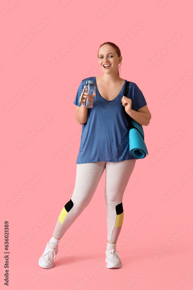 Portrait of sporty young woman with bottle of water and yoga mat on pink background