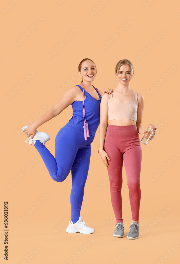 Sporty young women with bottle of water and skipping rope on beige background