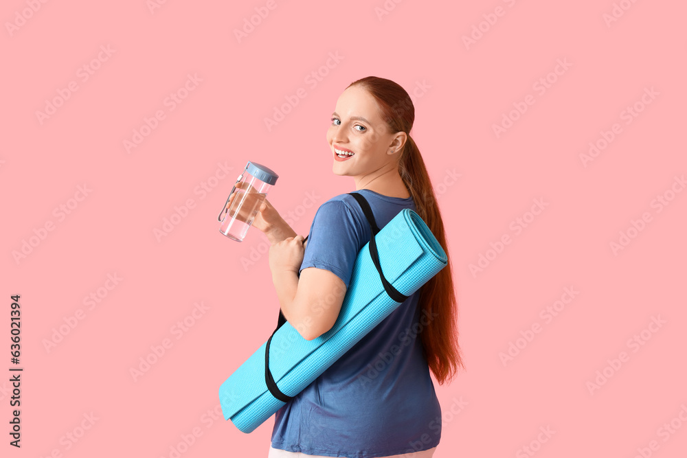 Portrait of sporty young woman with bottle of water and yoga mat on pink background