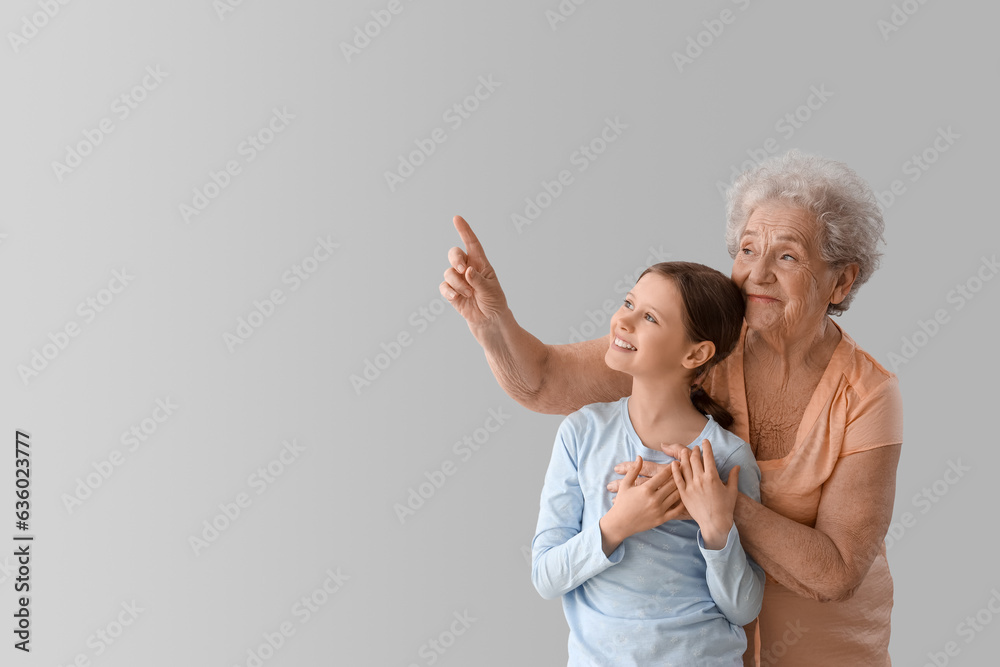 Little girl with her grandmother pointing at something on grey background