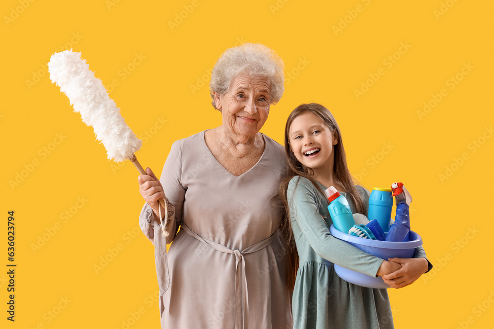 Little girl with her grandmother and cleaning supplies on yellow background