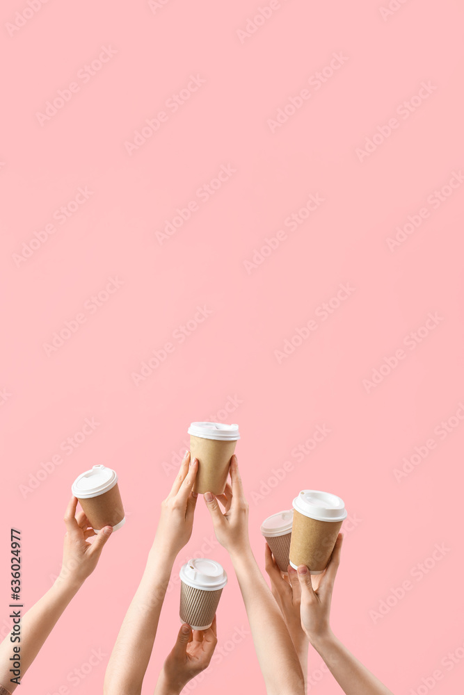 Female hands holding takeaway cups of coffee on pink background