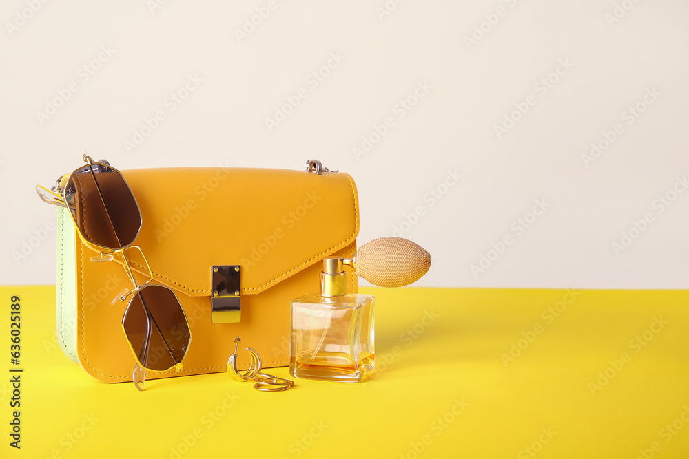 Stylish sunglasses with bag and perfume on yellow table