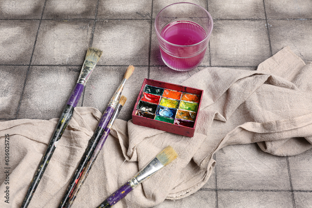 Artists paints with brushes, cloth and glass on grey tile background