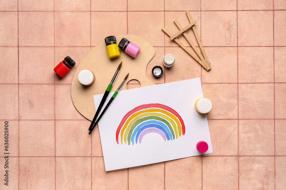 Drawing of colorful rainbow with artists palette, paints and brushes on beige tile background