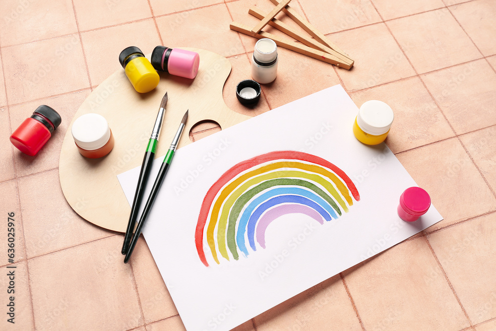 Drawing of colorful rainbow with artists palette, paints and brushes on beige tile background