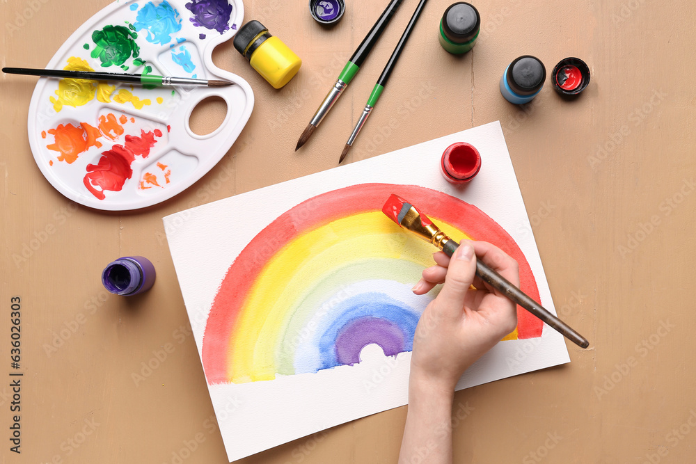 Female artist painting rainbow on beige background