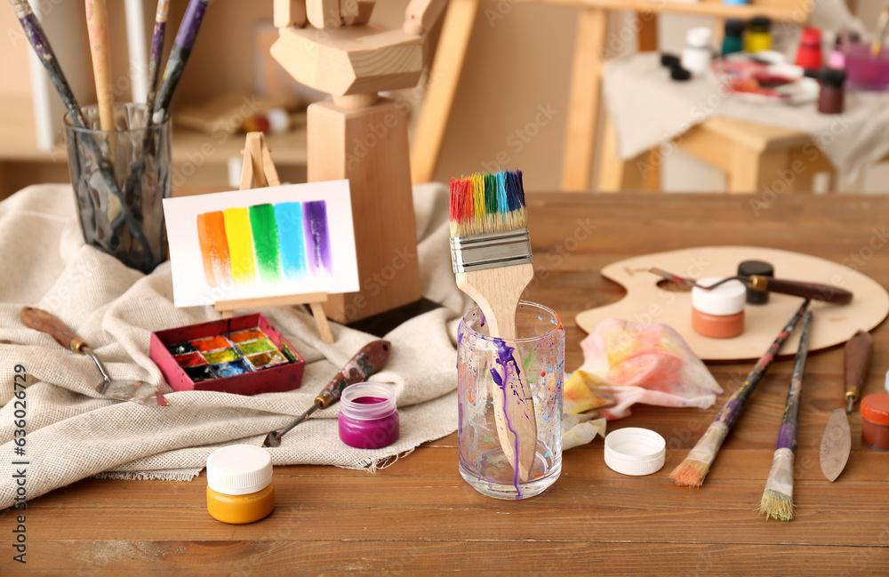 Glass with brushes, paints and mini easel in artists studio