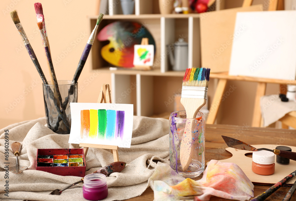 Glass with brushes, paints and mini easel in artists studio