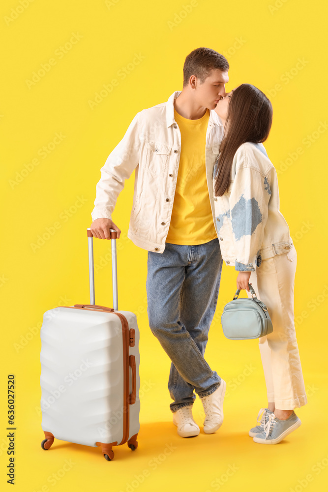 Happy young couple with suitcase kissing on yellow background