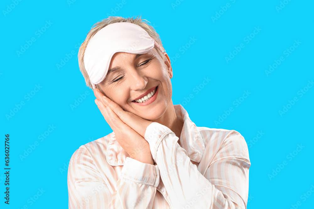 Mature woman in pajamas with sleeping mask on blue background, closeup