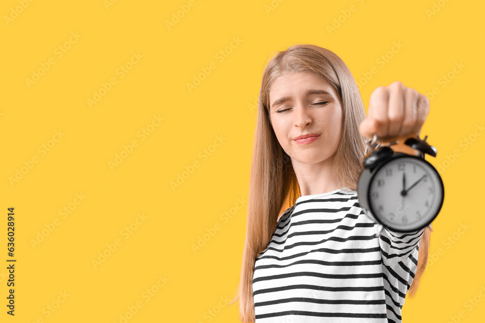 Stressed young woman with alarm clock on yellow background. Deadline concept