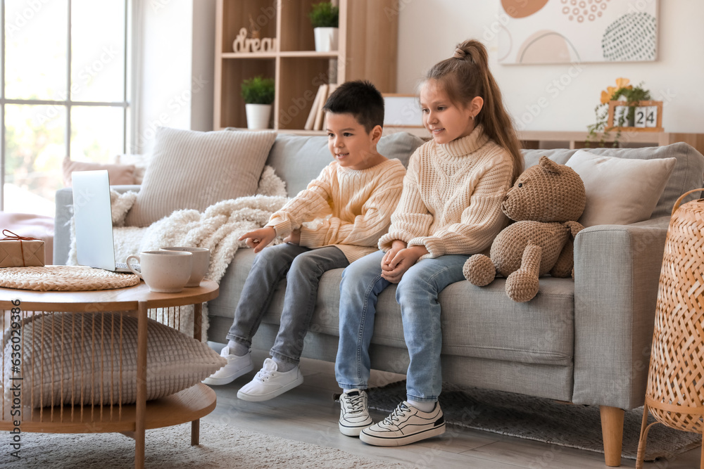 Cute little children in knitted sweaters watching cartoons at home