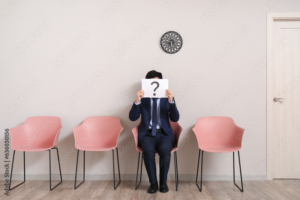 Male applicant holding paper sheet with question mark in room