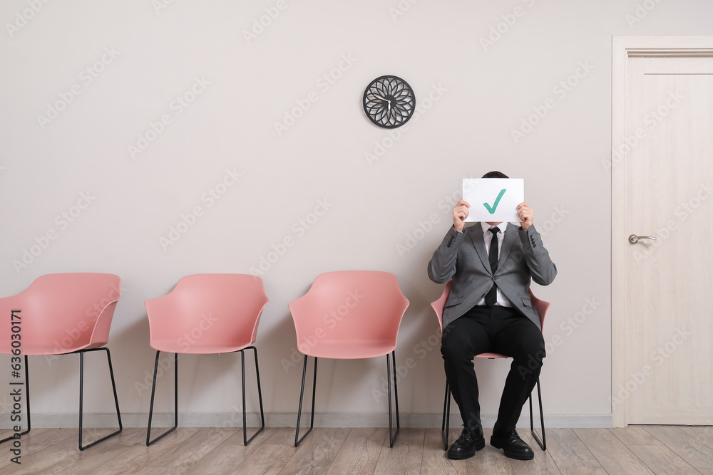 Male applicant holding paper sheet with check mark in room