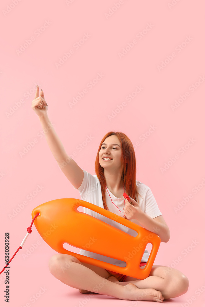 Female lifeguard with rescue buoy pointing at something on pink background