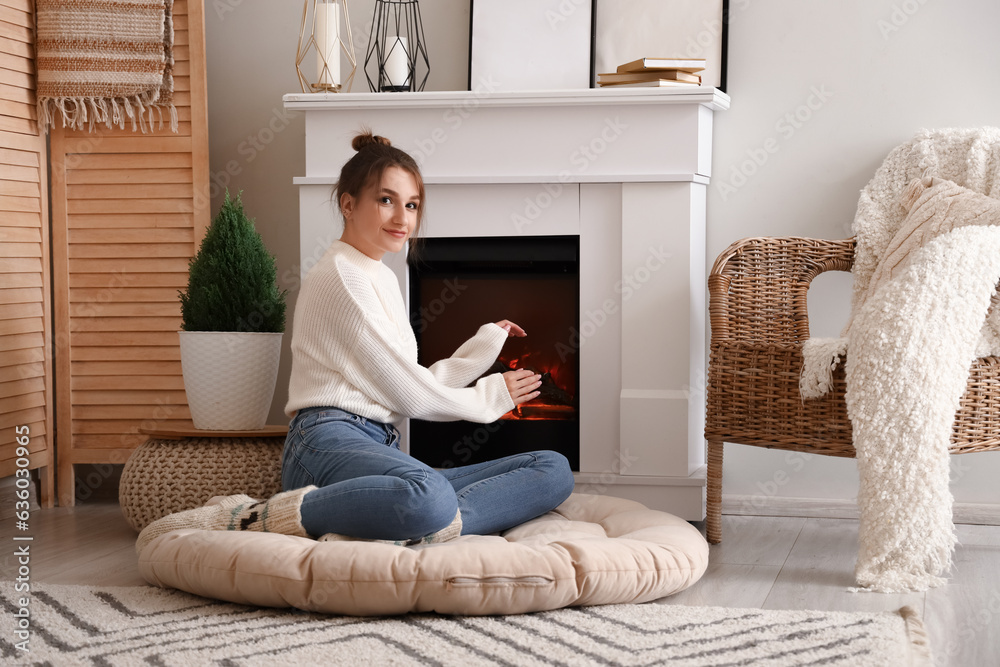 Young woman warming hands near fireplace at home