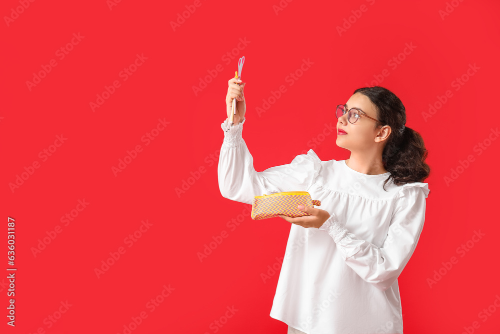 Female student with stationery and pencil case on red background