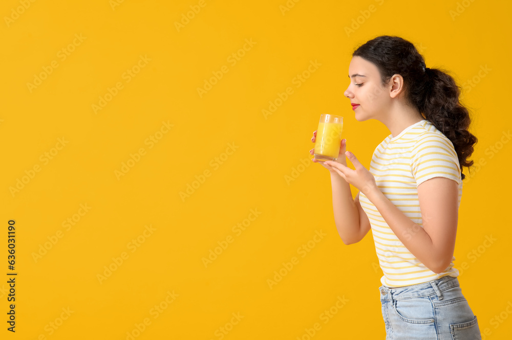 Teenage girl with glass of orange juice on yellow background