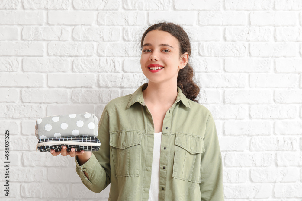 Female student with pencil cases on white brick background