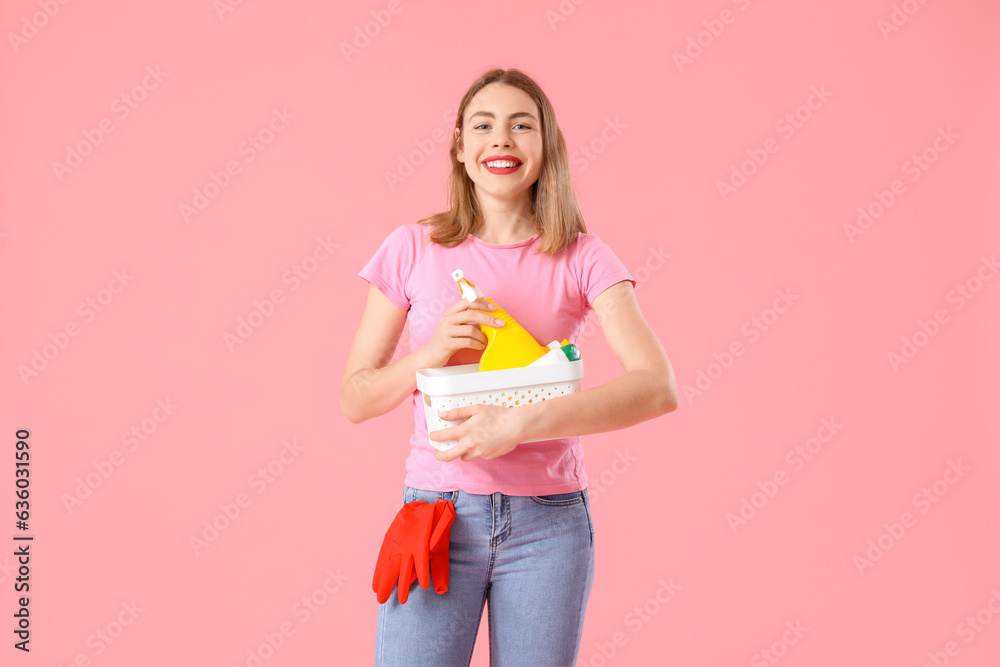 Young woman with cleaning supplies on pink background