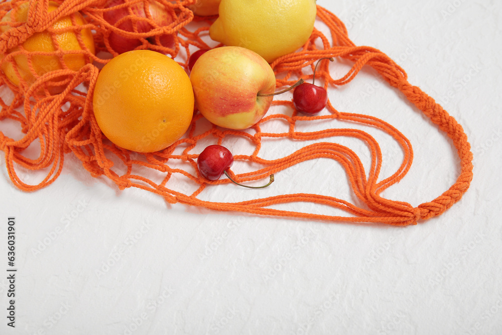 Mesh bag with fresh fruits on white background, closeup