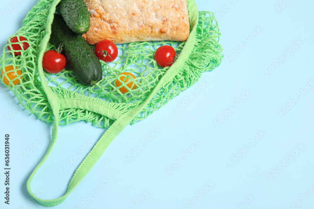 Mesh bag with fresh vegetables and bread on blue background, closeup