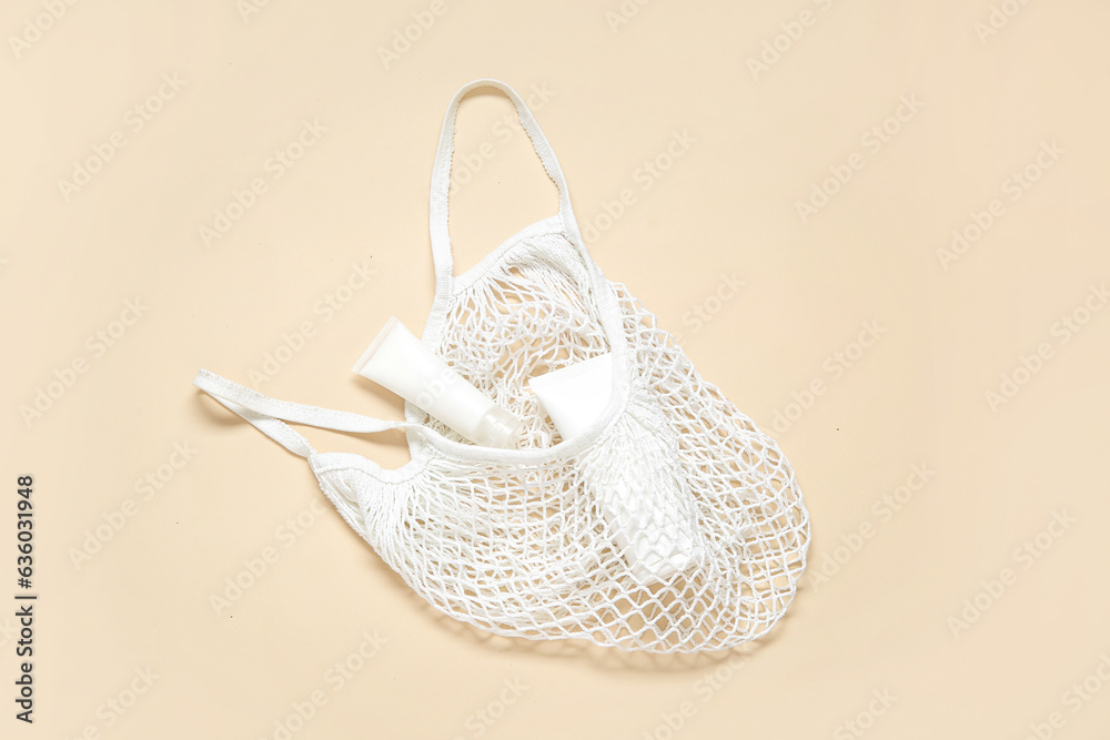 Mesh bag with tubes of cosmetic products on beige background