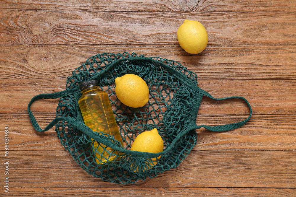 Mesh bag with fresh lemons and bottle of juice on wooden background